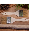 Two 2" Chip Brushes on a wood table, staged with a pinecone and faux greenery.