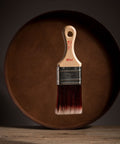 Paint brush with wooden handle and red bristle head floating in front of a dark brown circular platform.