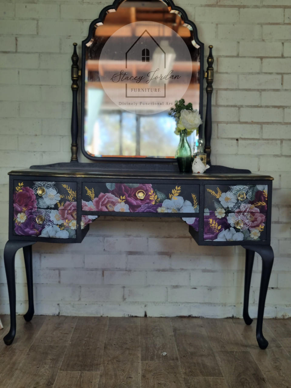 Belles and Whistles Botanical - Silkscreen Stencil provides an extra decorative touch to any project!
A black matte vanity with mirror the drawers cover in Floral Romance - Transfer and Botanical - Silkscreen Stencil is seen in gold accent around the transfer. Staged along a white brick wall and wooden floor.
