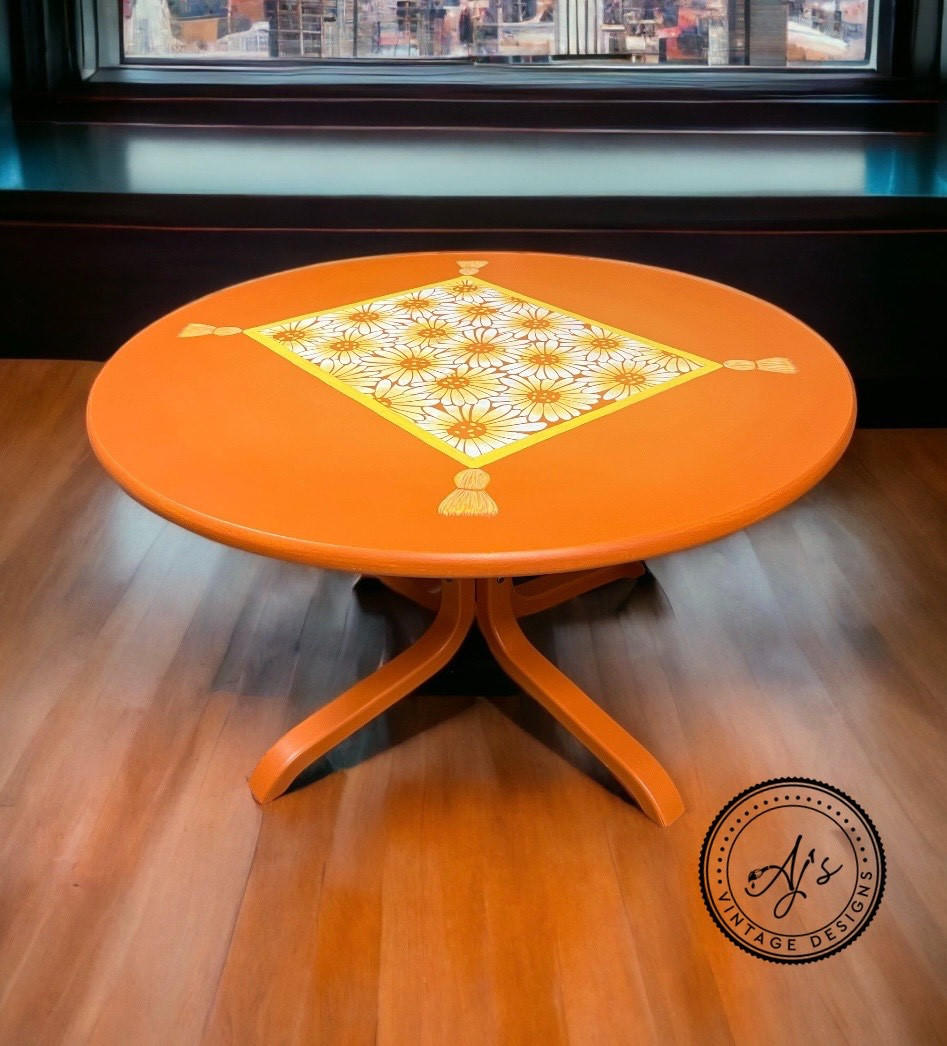 Orange painted table makeover. Crazy Daisy stencil applied on the table top in white, yellow, and orange with a yellow border. Yellow tassels painted on each corner of the border.