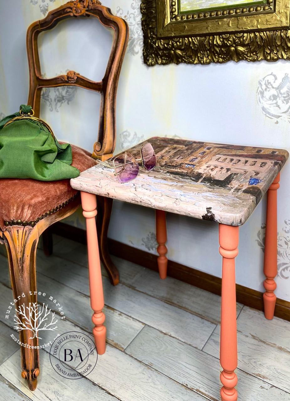 Belles and Whistles Gondola and Landscape - A1 Rice Decoupage Paper is a simple way to visually enhance any surface of your project! Cafe table wrapped with Gondola and Landscape - A1 Rice Decoupage Paper sealed with Dixie Belles Clear Coat in Satin with legs painted in Flamingo of the Dixie Belle Chalk Mineral Paint line. Staged next to vintage padded chair with a green drawstring bag on it and a pair of purple sunglasses on table on a off white wood floors and white with yellow striped wall.