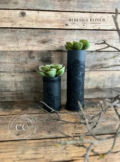 Two small black painted candle holders with succulents inside. Black Velvet Touch has been applied to the holders with the Mandala Silkscreen Stencil.