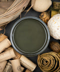 Dixie Belle Paint Collard Greens Chalk Mineral Paint is the perfect paint for any DIY project!
You are looking down on the Collard Green CMP so you can only see the paint in the can. The paint is sitting on a black surface with corks, grass basket and grass balls and wooden chatskis surrounding it.