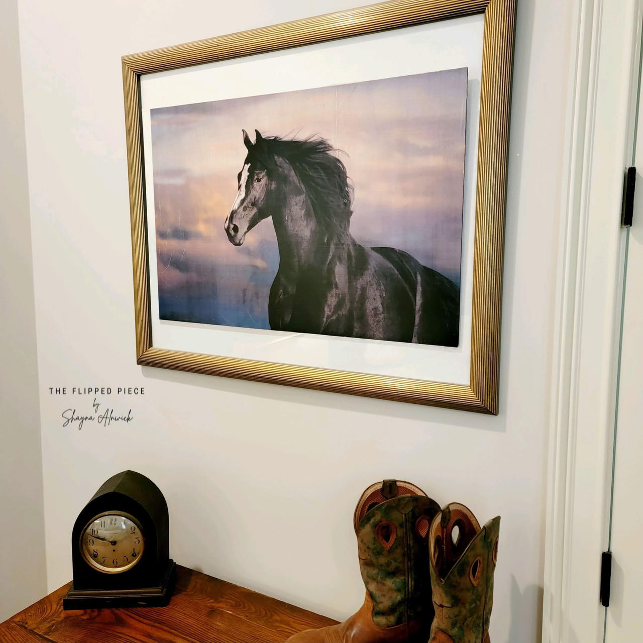 Majestic Horse decoupage paper in a gold frame, hung on the wall. Staged with cowboy boots and an old clock on the table below it.
