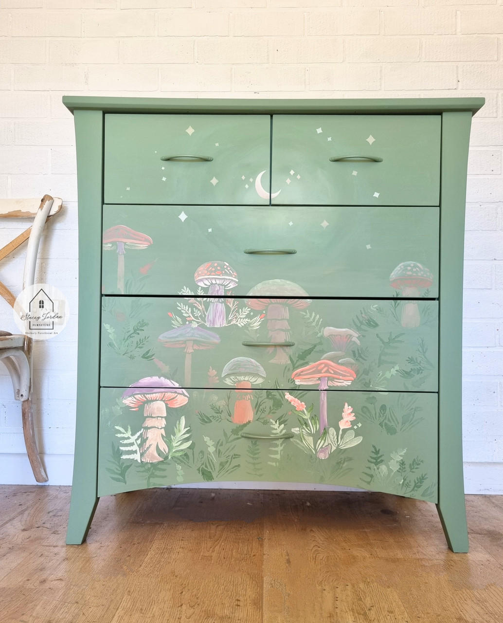 Green chalk painted dresser. 9 mushrooms with greenery, and a moon and stars on the top two drawers, applied with the Moonlit Mushrooms Stencil. The mushrooms are variations of purple, pink, green, and white.