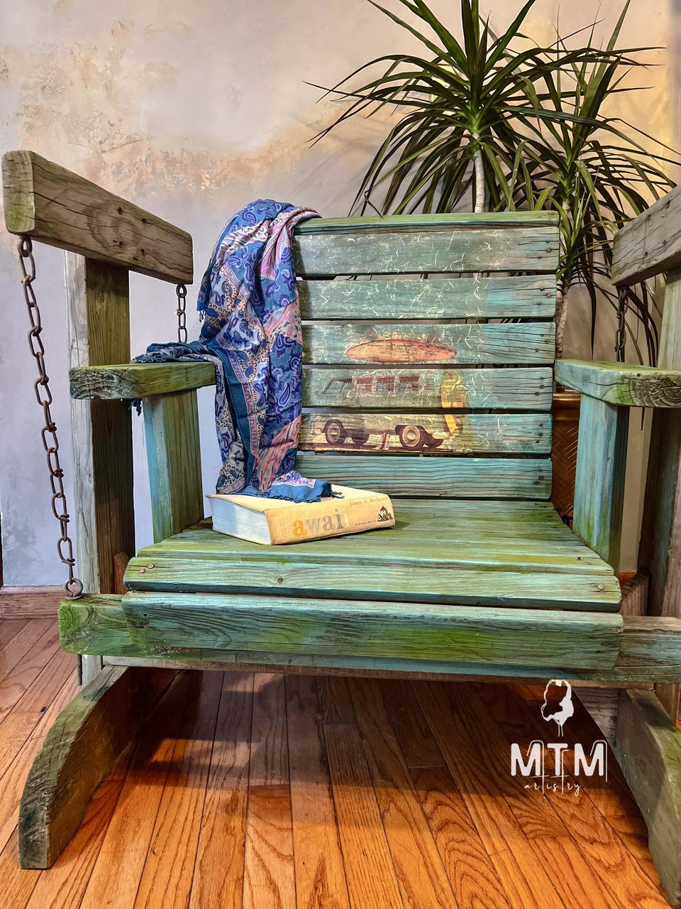 Rustic wooden porch swing type beach chair. The Surf's Up Decoupage Paper has been applied to the middle of the back of the chair and distressed. With a scarf draped over the back of the chair and a Hawaii book placed on the seat.