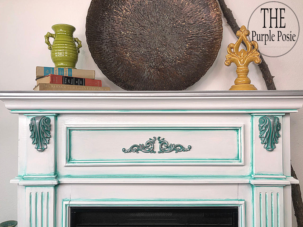 WoodUBend Applique #1361 (Set of 2) is the perfect mouldable embellishment for any project! This image shows Applique #1361 mounted on each side of a fireplace painted with Dixie Belle Chalk Mineral Paint. The fireplace is white with green accents. On the mantle are books, a vase and a metal tray.