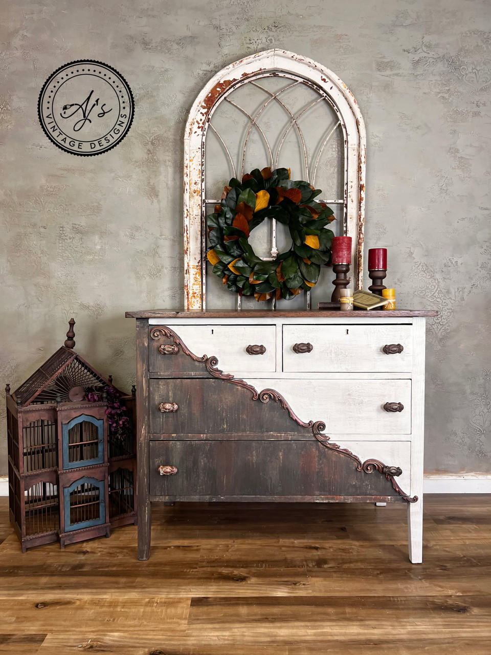 WoodUBend Applique #1723 (set of 2) is the perfect mouldable embellishment for any project!
A dresser with the Applique #1723 going diagonally across, corner to corner, dividing the two colors the piece is in, the one half is a rustic brown and the other side was white with brown hardware. Staged with a large bird cage house to the side of the dresser, on top of the piece is a leaf wreath .