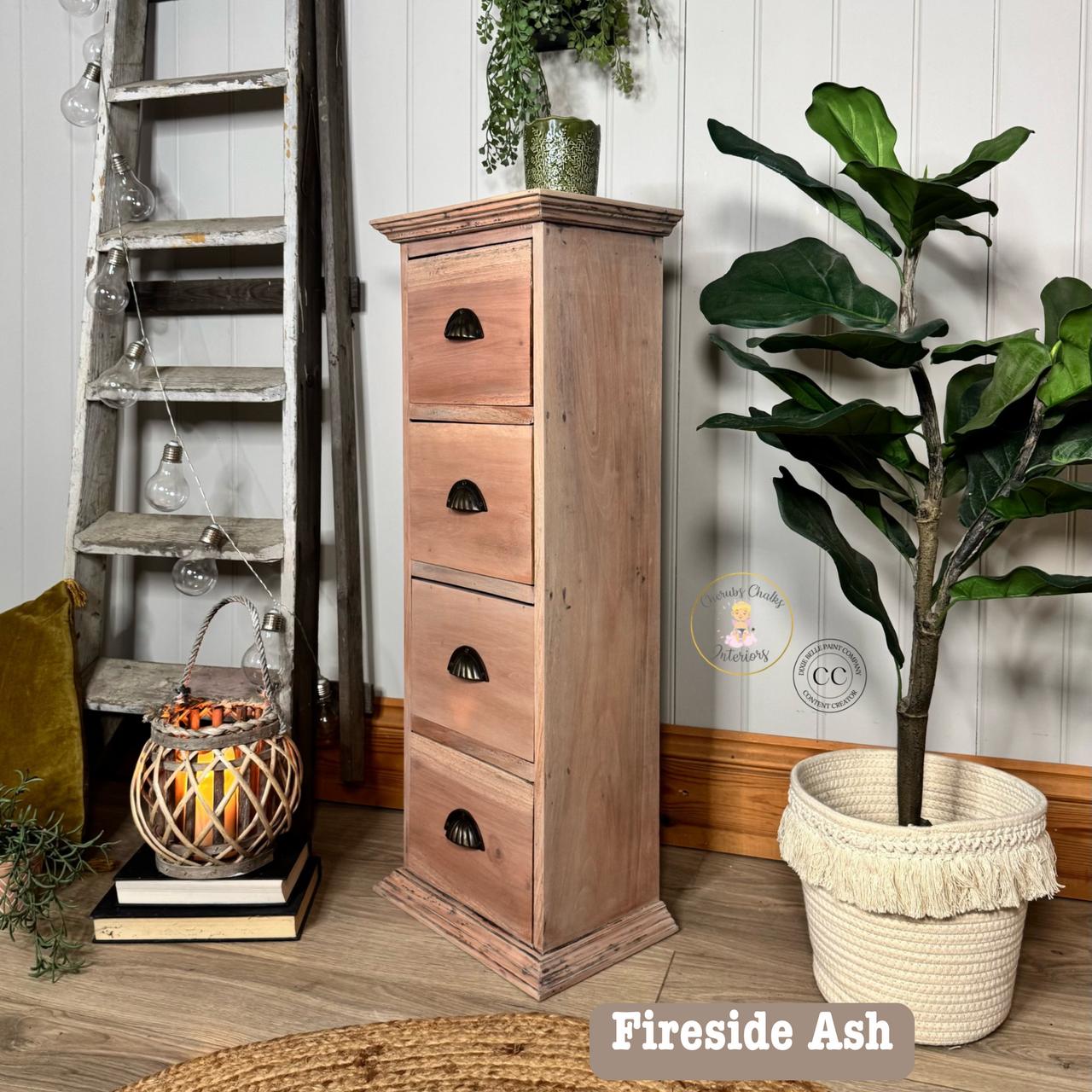A rustic wooden chest of drawers stands beside a green potted plant and a decorative basket with lights. A vintage ladder leans against the white paneled wall in the background. The setting is cozy and homely.