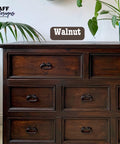 Dark wooden dresser with eight visible drawers, featuring metal handles. A label reading "Walnut" is visible. Potted plants are positioned on and beside the dresser. The text "FAFF designs" is in the top left corner.