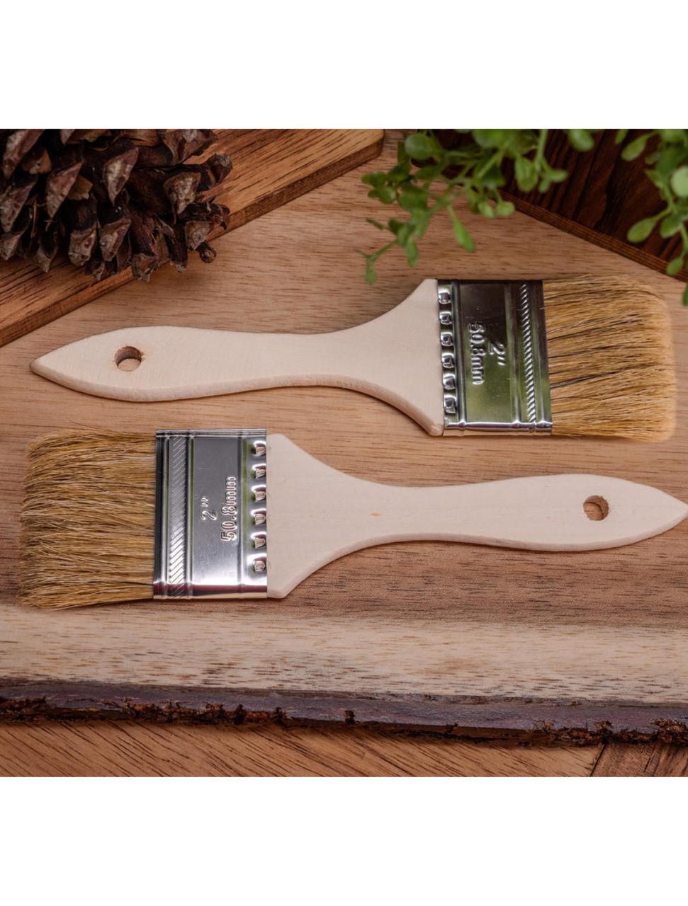 Two 2" Chip Brushes on a wood table, staged with a pinecone and faux greenery.