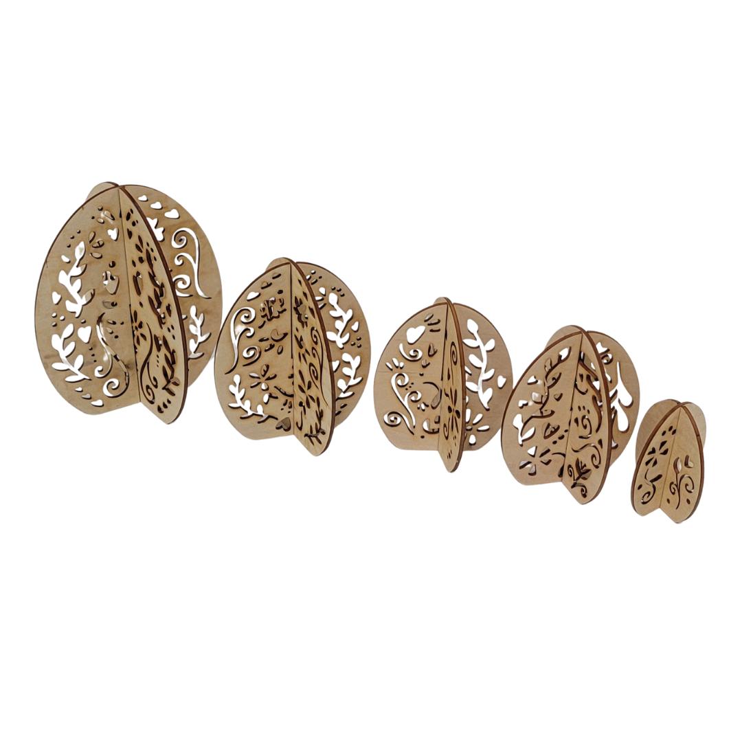 A set of five intricately carved wooden egg cutouts of varying sizes, arranged in a line from largest to smallest. Each piece features detailed floral and vine cut-out patterns.