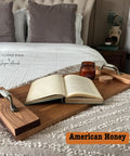 A cozy bedroom scene with an open book on a wooden tray positioned on a textured bedspread. A lit candle and a cork coaster are also on the tray. A bed with tufted pillows is in the background. Text reads "American Honey."