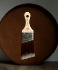 Paint brush with wooden handle and red bristle head floating in front of a dark brown circular platform.