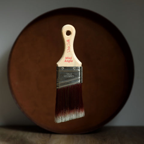 Paint brush with wooden handle and red bristle head floating in front of a dark brown circular platform.