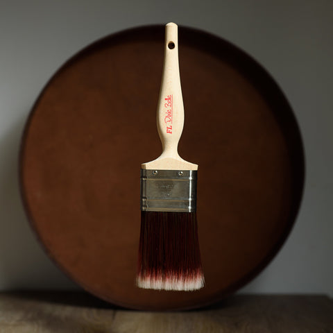 Paint brush with wooden handle and red bristle head floating in front of a dark brown circular platform.
