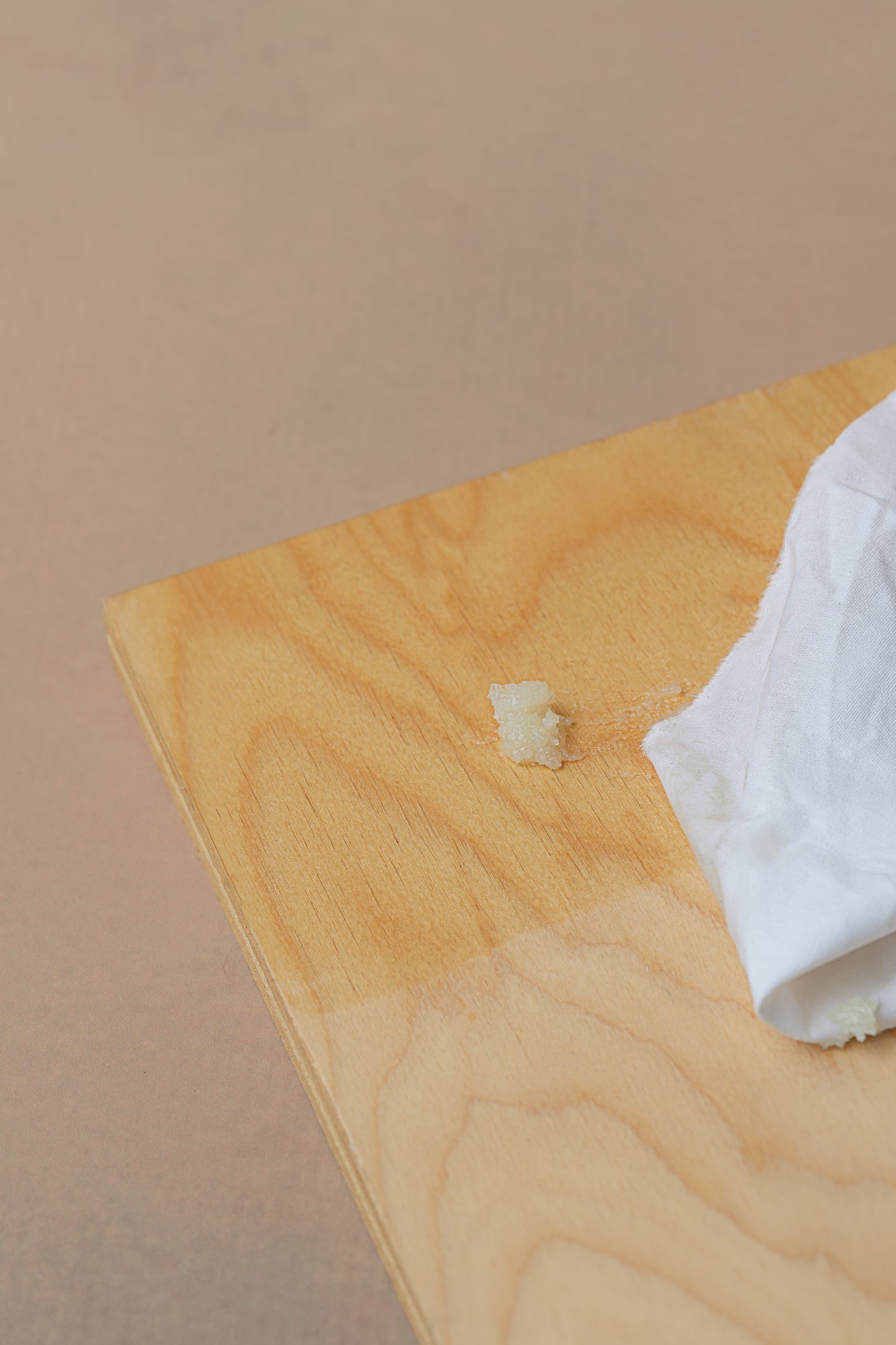 A small dab of wood conditioner sits on a light wooden surface next to the edge of a white cloth.