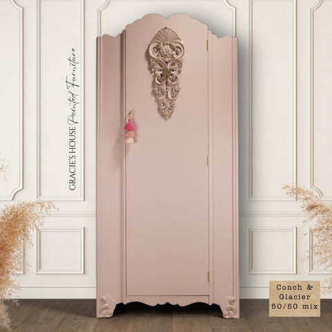 Conch Silk All-In-One paint is perfect for painting kitchen cabinets, bathroom cabinets and painting furniture
A vintage-style wardrobe painted in a soft pink shade, with ornate floral carvings at the top center and corners. Small tassels hang from the knob. Decorative text on the left reads “Gracie’s House Painted Furniture.” A beige swatch reads “Conch & Glacier 50/50 mix.”.