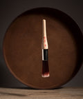 Paint brush with wooden handle and red bristle head floating in front of a dark brown circular platform.
