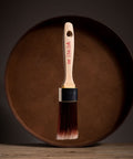 Paint brush with wooden handle and red bristle head floating in front of a dark brown circular platform.