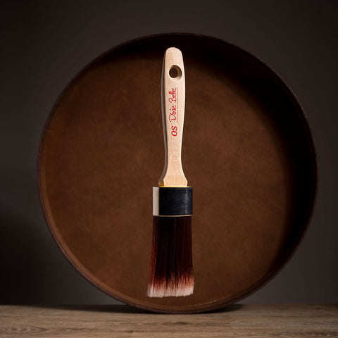 Paint brush with wooden handle and red bristle head floating in front of a dark brown circular platform.