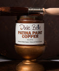 Jar of Dixie Belle Patina Paint Copper with a brush on a dark background
