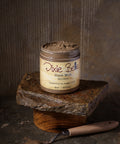 A jar of Dixie Belle Dixie Mud Brown sits on a stone slab and wooden base. The label reads "Straight from the swamps of Dixie" and indicates the container holds 8oz (237mL) of product.