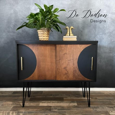 A side table chalk painted in black chalk paint with two sliding drawers.  with wood not painted, plant on top and a book with two duck heads for staging