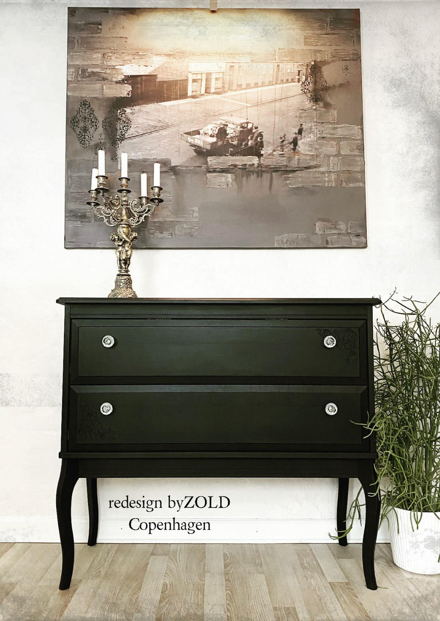 side table with two drawers, painted in a dark black all in one paint, staged with a candelabra on top and a picture on the wall of an old time city with truck and people.