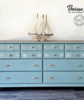 A chalk painted dresser in blue chalk paint, stenciled top drawers, staged with a sailboat on top.