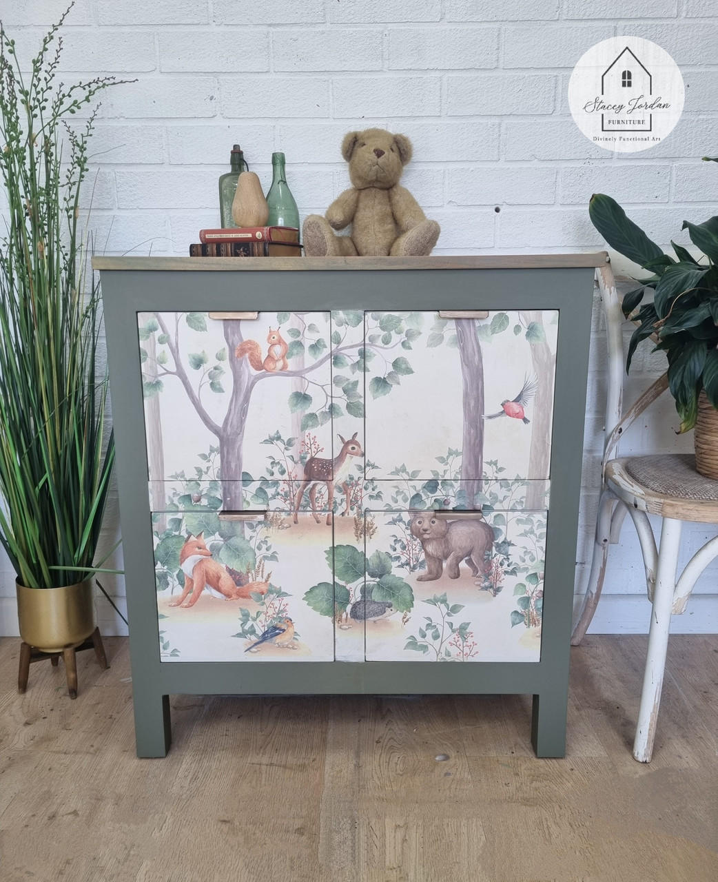 Belles and Whistles Woodland Nursery - A1 Rice Decoupage Paper.  Small side table with Woodland Decoupage Rice paper applied staged with teddy bear and books and bottles on top and a plant in gold vase on left side and chair with plant on right side