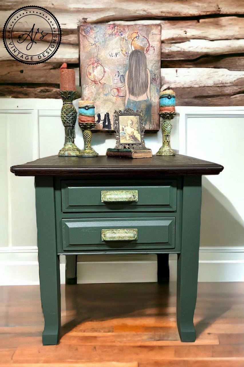 Dark green painted nightstand makeover with a dark wood top. Staged with 3 candlesticks, books and a picture frame on top, and a painting of a mermaid hanging on the wall behind the piece.