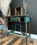 Dark green painted desk makeover with wooden spindles and two lit candlesticks on top. Staged next to a vase full of long feathers.