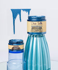 Two containers of Dixie Belle Moonshine Metallics paint in Pacific blue sit on a reflective surface. Showing paint dripping from a clear sheet above.