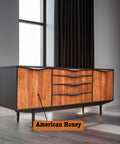 A mid-century modern sideboard with a sleek design, featuring a dark frame and vibrant wooden fronts labeled as "American Honey." It stands on tapered legs and is positioned near a large window with closed black curtains.
