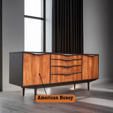 A mid-century modern sideboard with a sleek design, featuring a dark frame and vibrant wooden fronts labeled as "American Honey." It stands on tapered legs and is positioned near a large window with closed black curtains.