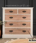 A wooden dresser with a light cream frame and natural wood drawers, featuring ornate metal handles. It's set against a dark paneled wall, accompanied by a basket with a plant and a terracotta pot on a light rug. A label reads "Au Naturel."