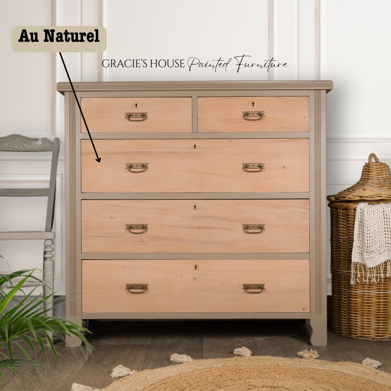 A wooden chest of drawers with a natural finish stands against a white wall. It has three large drawers and two small top drawers. A woven basket is next to it on the right, and a chair is on the left. Text on the image reads: "Gracie's House Painted Furniture."