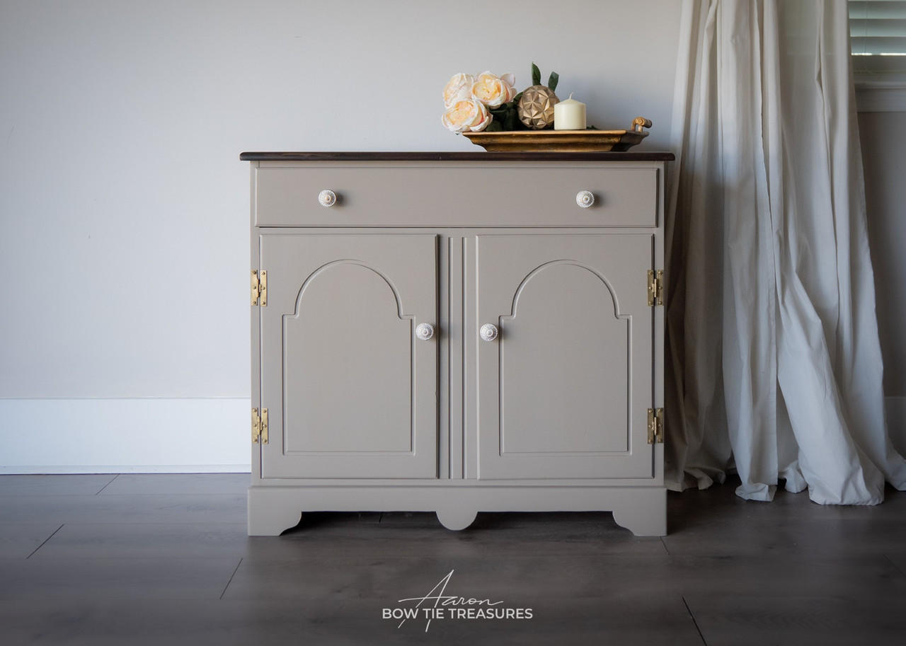 Beige painted buffet makeover with gold hinges and white knobs. Staged with a wooden platter with flowers and a candle on top.