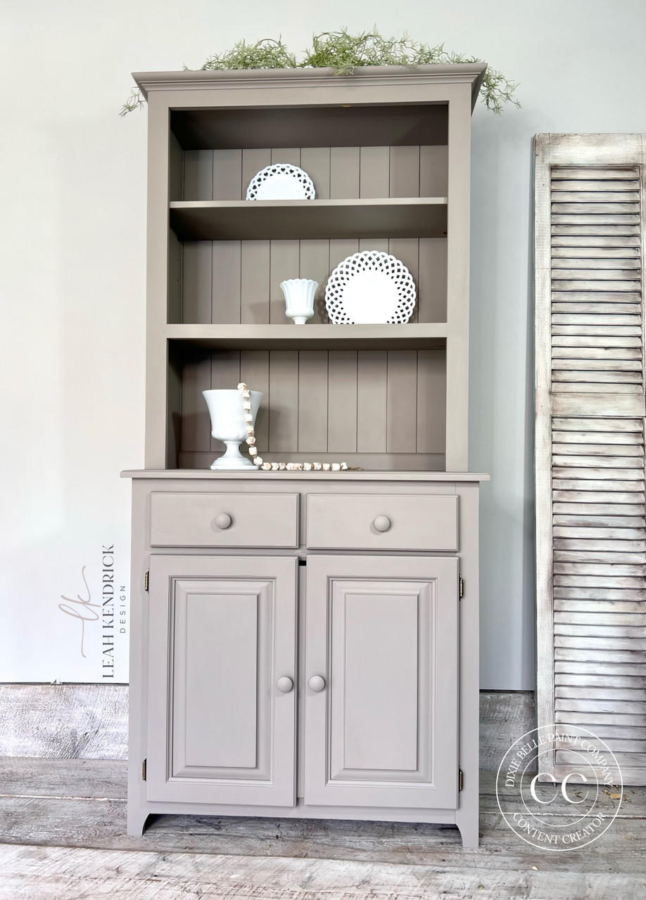 Beige painted hutch makeover. Staged with white plates and cups inside the open cabinets.