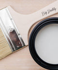 Belles and Whistles Big Daddy Brush. the Big Daddy Brush places on a wooden background with white chalk paint besides brush.