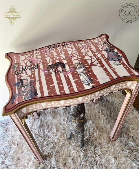 Belles and Whistles Birchwood - Stencil provides an extra decorative touch to any project! Pink table with the Birchwood - Stencil as the base with  Alice Part 2 - Transfer on top to give it a fairytale look. Staged on a furry carpet and statue underneath table.