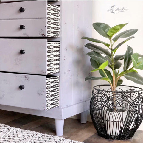Belles and Whistles Botanical - Silkscreen Stencil provides an extra decorative touch to any project!
A dresser in a white farmhouse distressed style with opened drawers, on the side of these drawers are the Botanical - Silkscreen Stencil. Staged next to a potted plant .