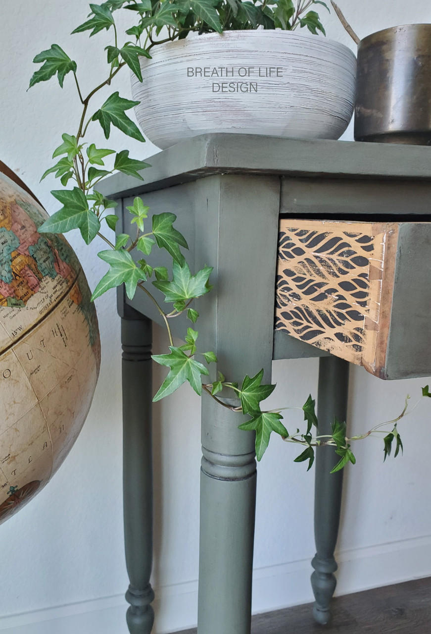 Belles and Whistles Botanical - Silkscreen Stencil provides an extra decorative touch to any project!
The side of a console table with the drawer open, on the side of these drawers is the Botanical - Silkscreen Stencil. Staged with a white bowl, greenery and a cut off Globe.