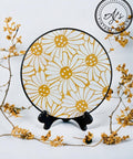 Crazy Daisy stencil applied on a plate in white and yellow with a black rim. Placed on a black plate holder. On a white background with yellow flowers strewn around.
