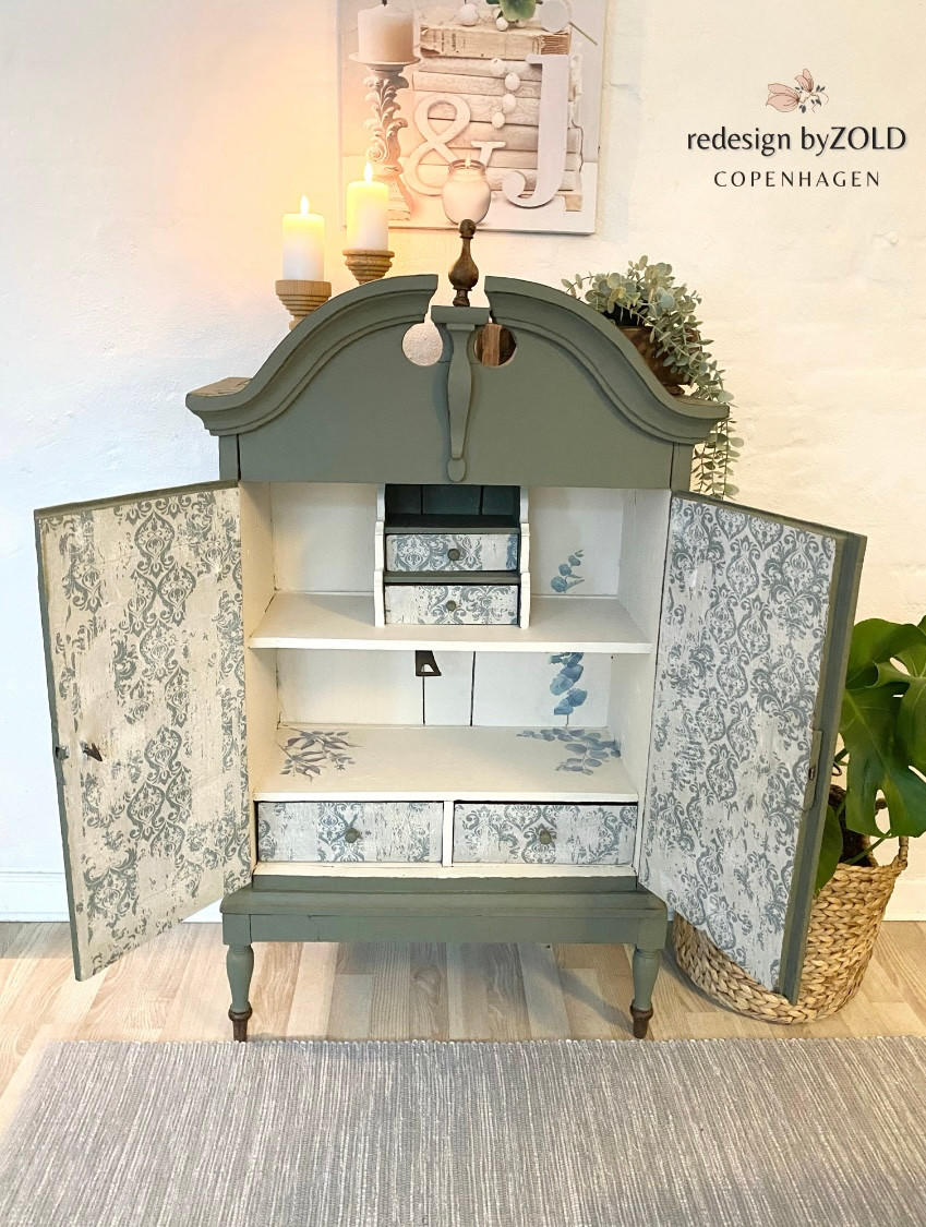 Belles and Whistles Distressed Damask - A1 Rice Decoupage Paper 
There is a medium-sized armoire with it's two, front doors open displaying the inside of the doors as well as the front of 4 of the drawers inside the armoire have distressed-damask decoupage on them. It is staged with lit candles, plants and picture on the wall behind.