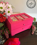 Belles and Whistles Dixie Shine 
Hot pink jewelry box with Dixie Shine in Silver on woodwork on top of piece. Staged with greenery and flowers around piece.