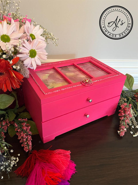 Belles and Whistles Dixie Shine 
Hot pink jewelry box with Dixie Shine in Silver on woodwork on top of piece. Staged with greenery and flowers around piece.