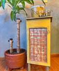 Yellow and orange painted cabinet with tannish brown legs. Don't Be Square Stencil was applied in silver on the front of the cabinet door.