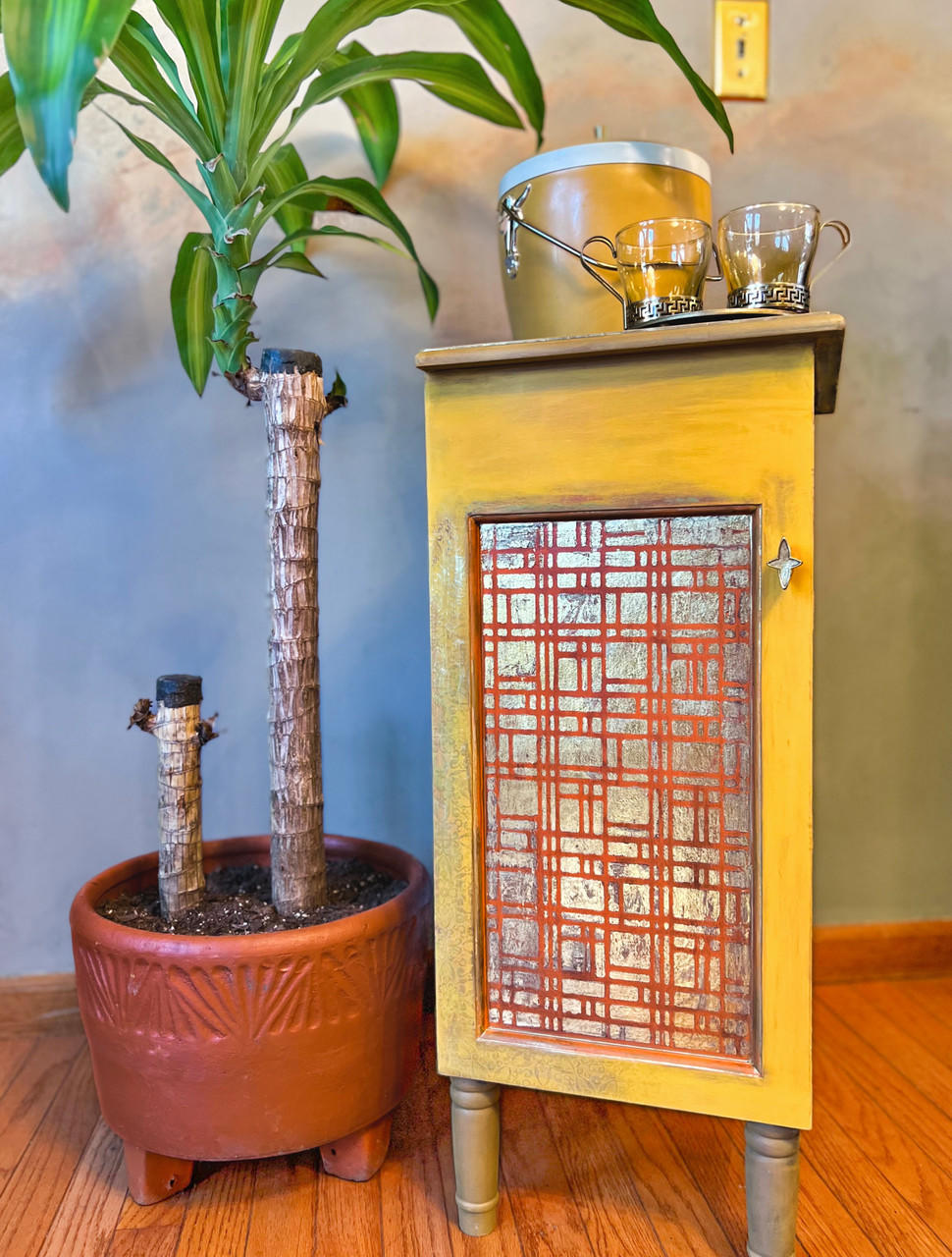 Yellow and orange painted cabinet with tannish brown legs. Don't Be Square Stencil was applied in silver on the front of the cabinet door.
